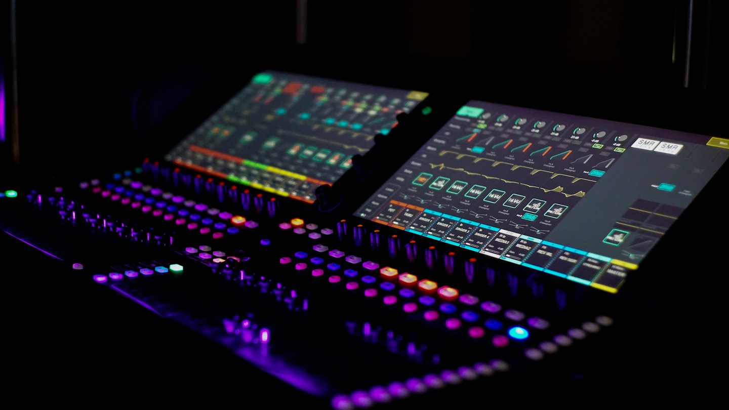 Console de mixage audio professionnelle avec boutons lumineux et formes d'onde numériques.