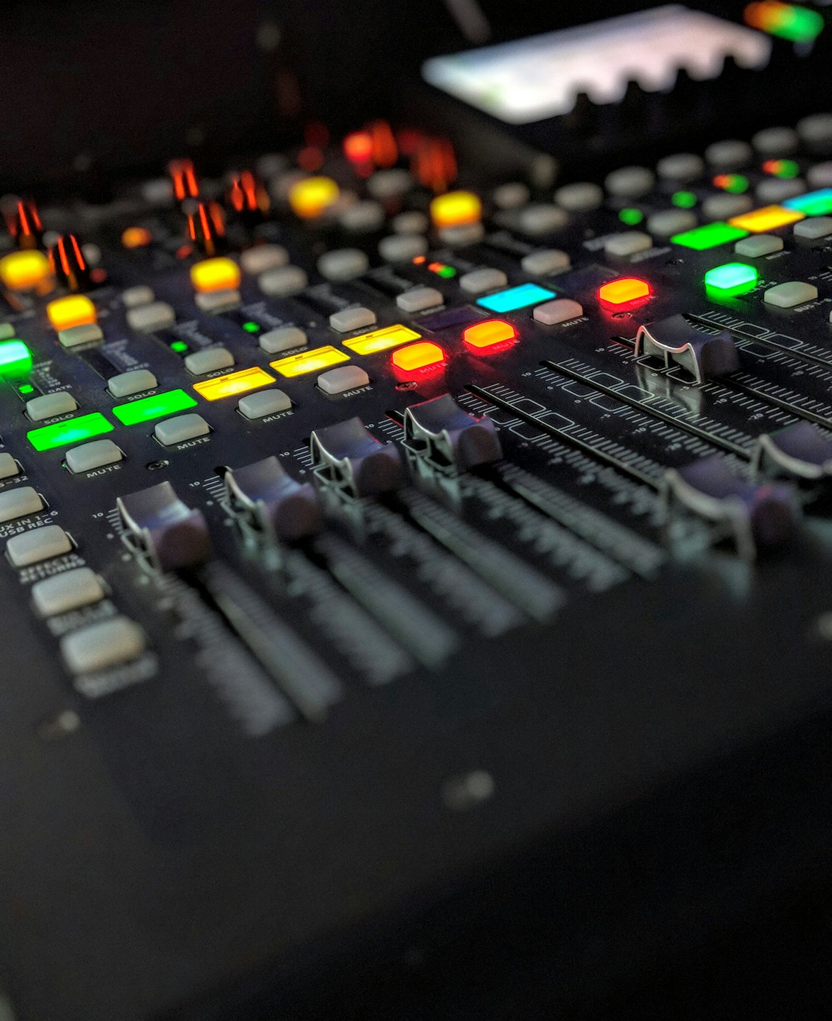 Console de mixage audio professionnelle avec boutons et faders illuminés.